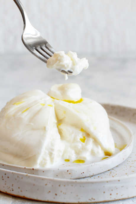 Burrata came about as a way to reduce waste when making mozzarella. Warm mozzarella cheese is stretched around leftover mozzarella curds, or stracciatella. Then cream is added to the curds before the mozzarella shell is tied in a knot.